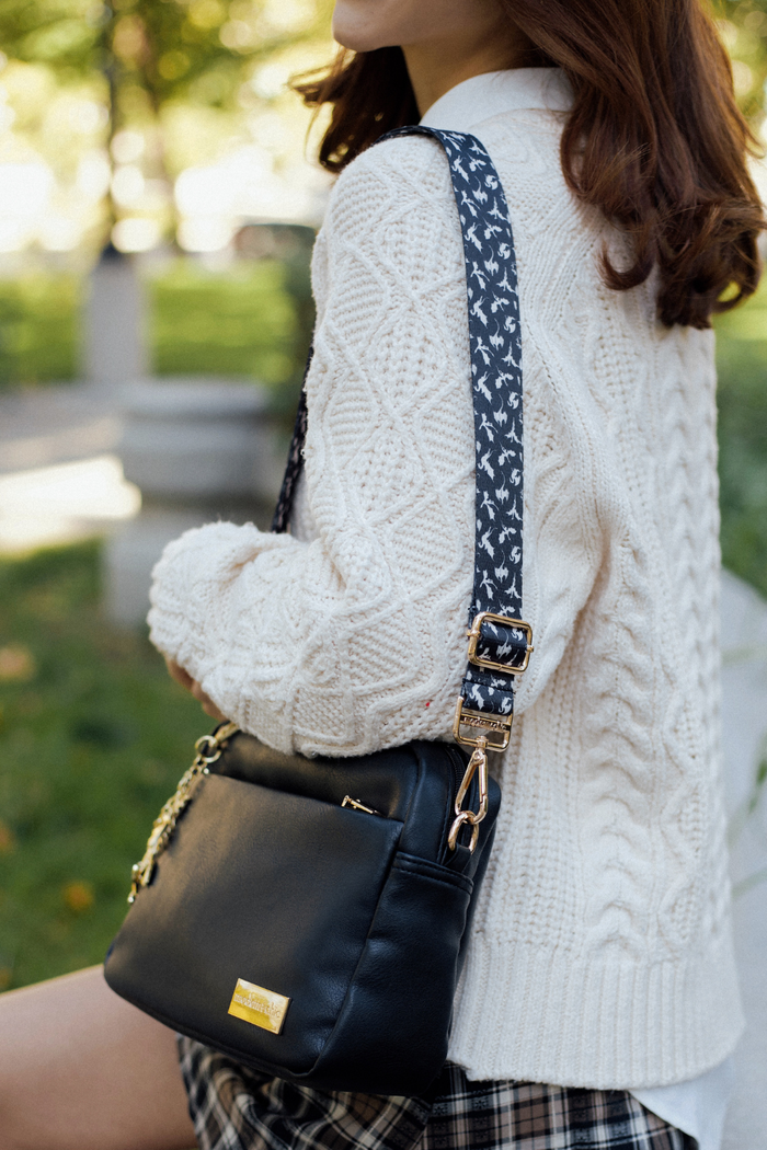 Person wearing a white cable-knit sweater, a black handbag, and a black-and-white dragon strap.