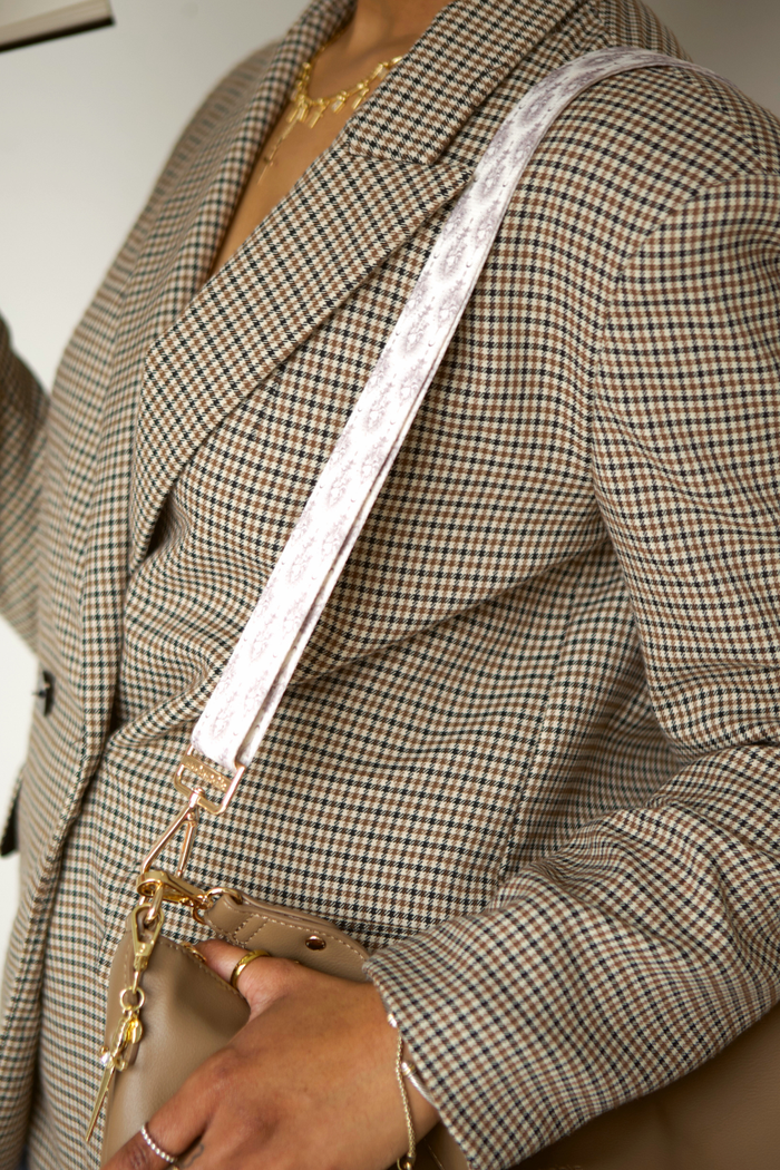 Person wearing a checkered blazer with a beige handbag, sword-patterned strap, and a sword charm.