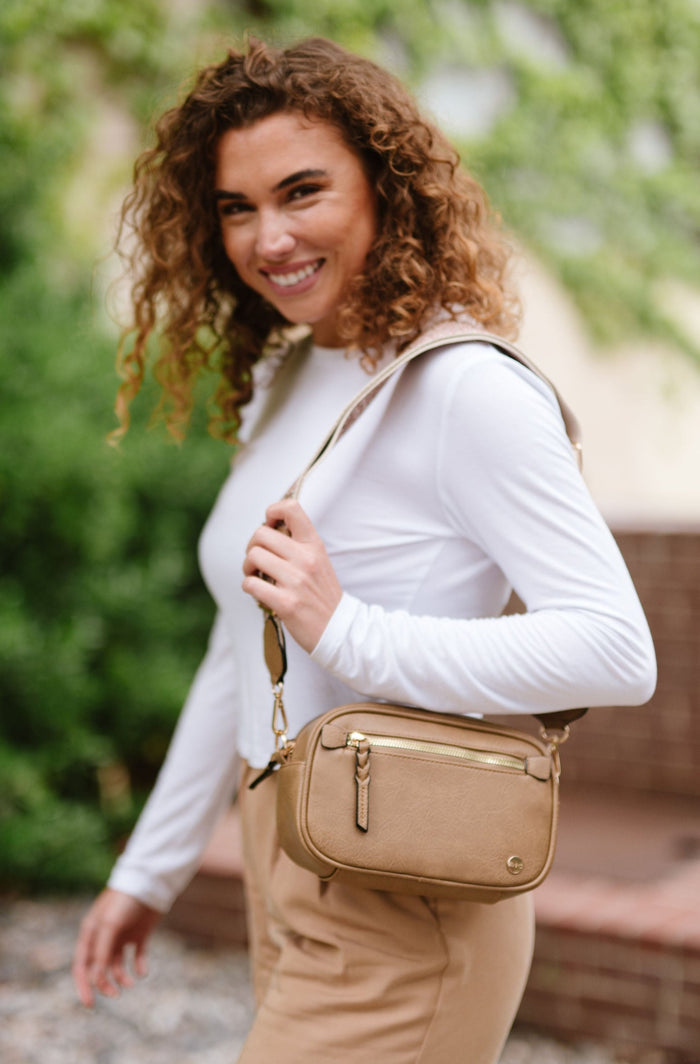 Woman wearing white shirt, tan pants and a Modern + Chic Gentry Vegan Leather Crossbody Bag in tan.