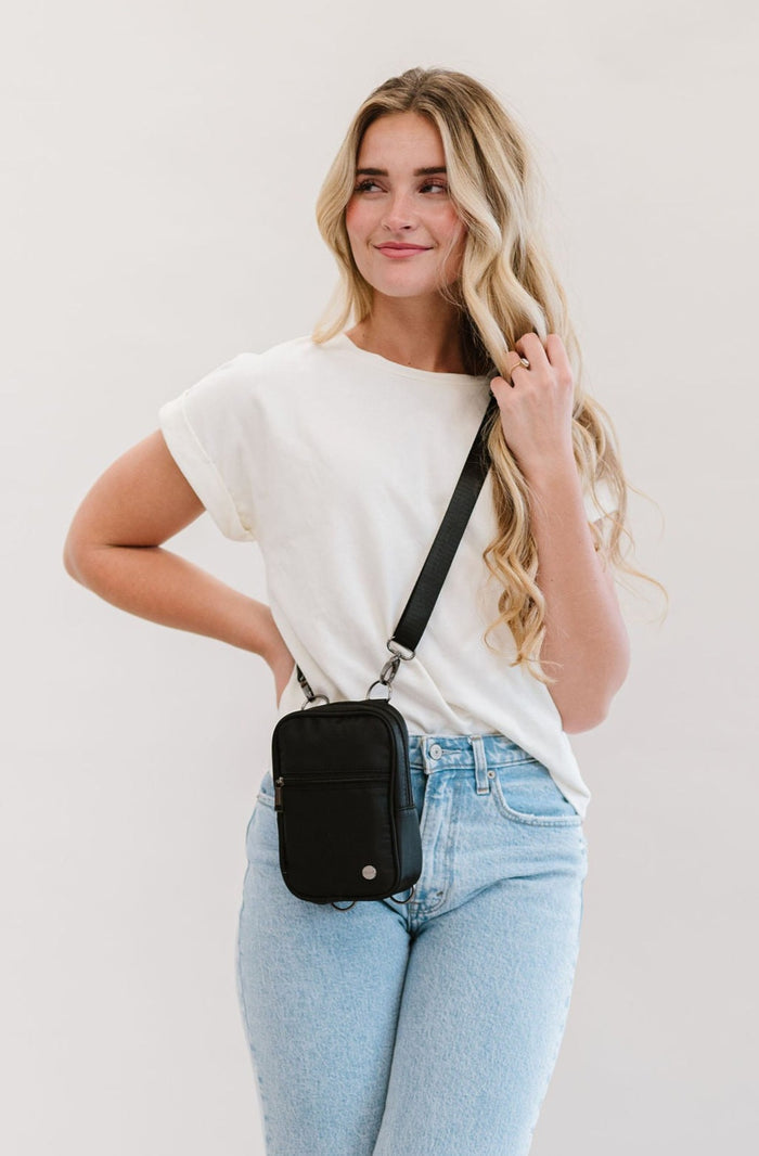 A woman wearing a black Modern + Chic Lainey Convertible Crossbody Bag for Women with a white top and jeans.