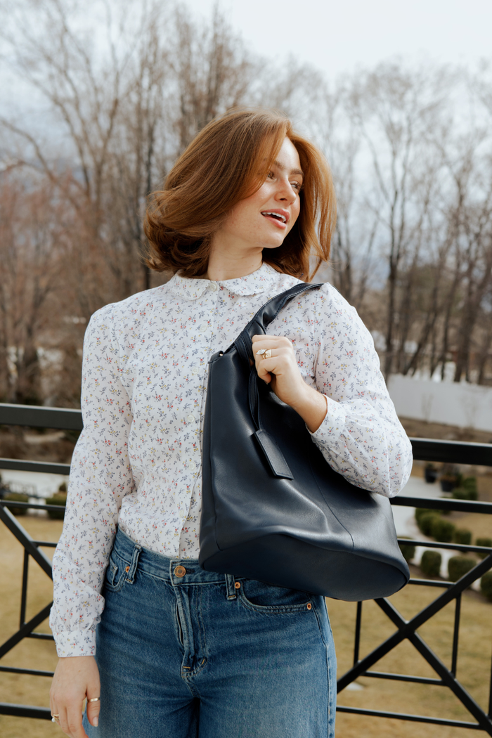 A woman wearing a floral white button up shirt with jeans and a black Modern+Chic Olivia Convertible Slouchy Tote Bag for Women over her shoulder.