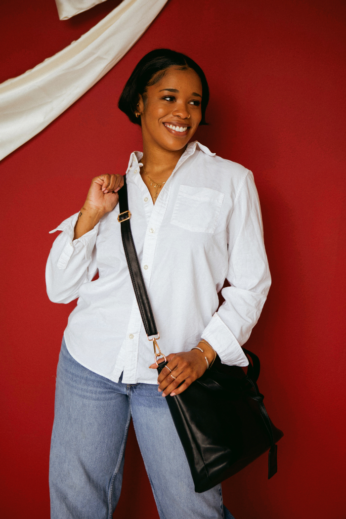 A woman wearing a white button up shirt with jeans and a black Modern+Chic Olivia Convertible Slouchy Tote Bag for Women across her body.