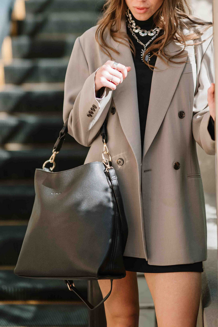 Woman holding a black Modern+Chic Sawyer Convertible Slouchy Tote Bag for Women with a vegan leather braided shoulder strap as a longer crossbody strap hangs.